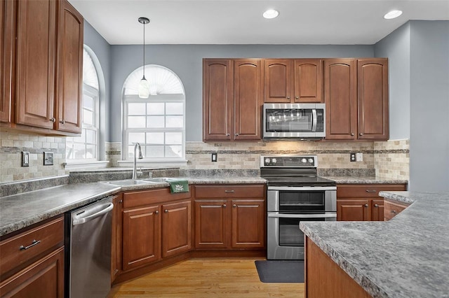 kitchen featuring appliances with stainless steel finishes, sink, decorative backsplash, hanging light fixtures, and light hardwood / wood-style flooring