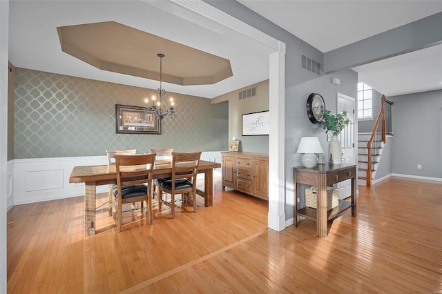 dining room with a notable chandelier, light hardwood / wood-style floors, and a tray ceiling