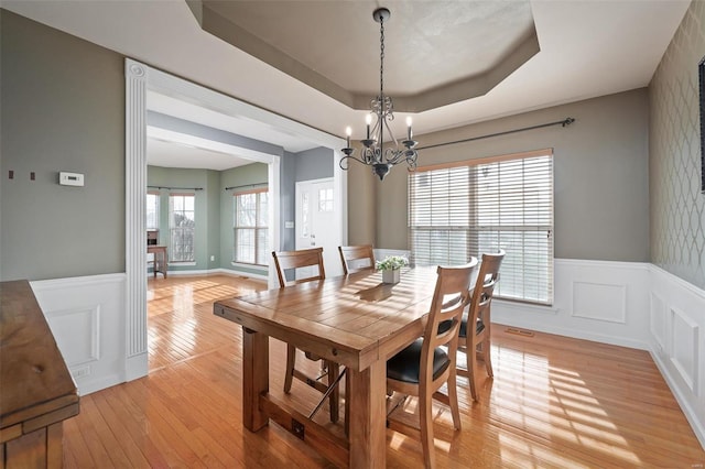 dining space with an inviting chandelier, light hardwood / wood-style flooring, and a raised ceiling