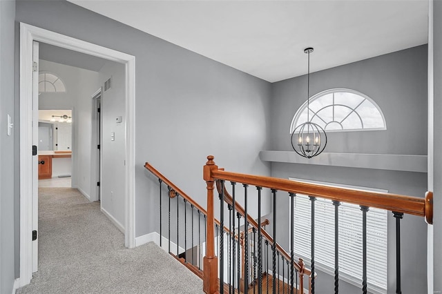 hallway with light colored carpet and a chandelier