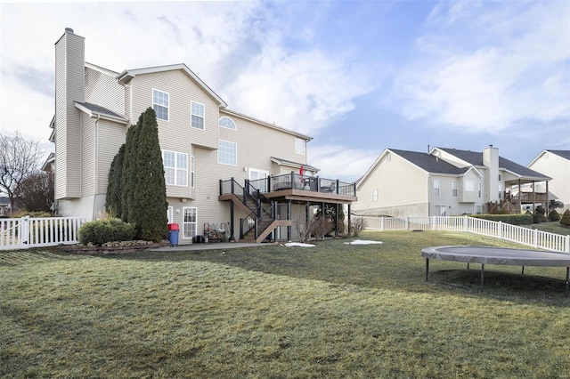 rear view of house featuring a deck, a yard, and a trampoline