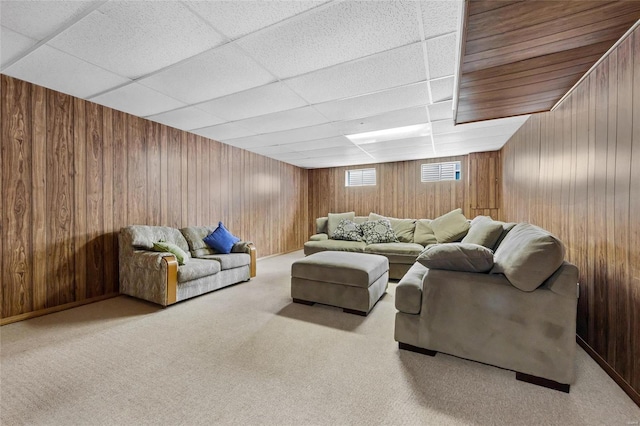 carpeted living room featuring a drop ceiling and wood walls