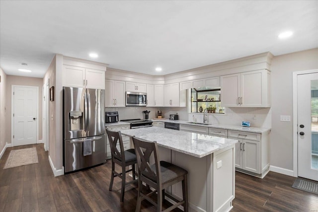 kitchen with a center island, appliances with stainless steel finishes, white cabinetry, and light stone counters