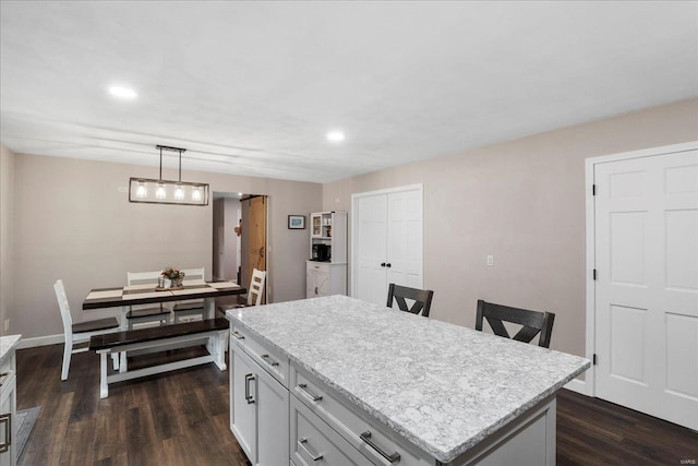 kitchen with white cabinetry, a kitchen island, dark hardwood / wood-style floors, decorative light fixtures, and light stone countertops