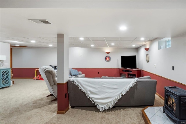 living room with light carpet, a wood stove, and a drop ceiling