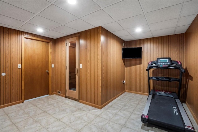 workout room featuring a paneled ceiling and wooden walls