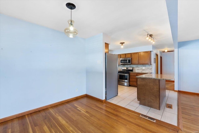 kitchen with light stone counters, tasteful backsplash, light wood-type flooring, appliances with stainless steel finishes, and pendant lighting