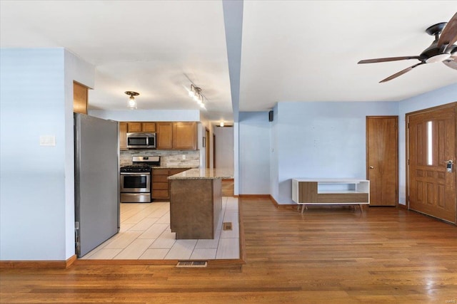 kitchen featuring ceiling fan, appliances with stainless steel finishes, backsplash, light stone counters, and light wood-type flooring