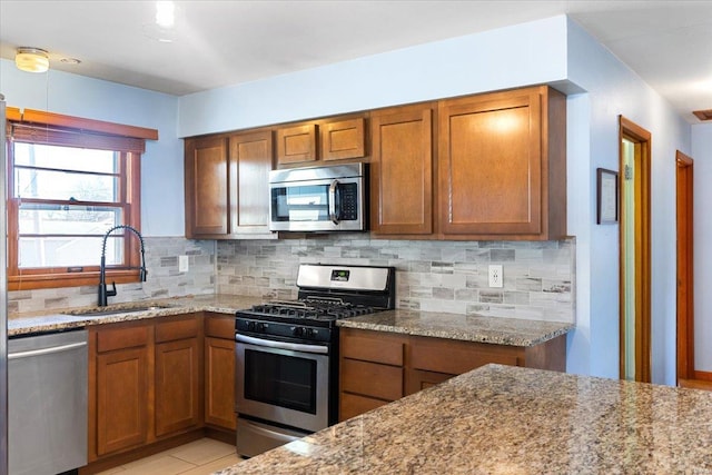 kitchen with stainless steel appliances, tasteful backsplash, sink, and light stone counters