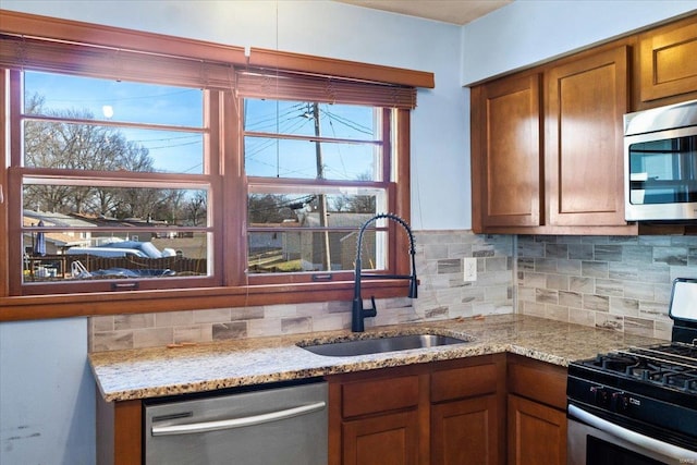 kitchen with light stone counters, sink, decorative backsplash, and stainless steel appliances