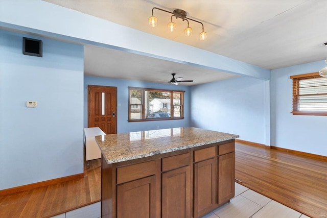 kitchen with light stone counters, light wood-type flooring, ceiling fan, and a kitchen island