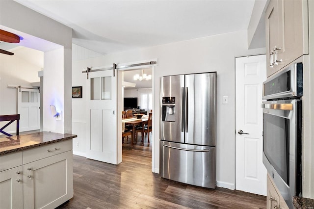 kitchen featuring a barn door, dark hardwood / wood-style floors, dark stone counters, and appliances with stainless steel finishes