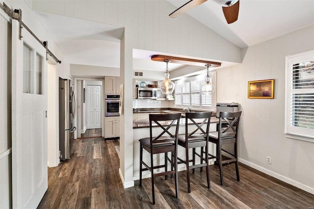 kitchen with plenty of natural light, a breakfast bar area, hanging light fixtures, stainless steel appliances, and a barn door