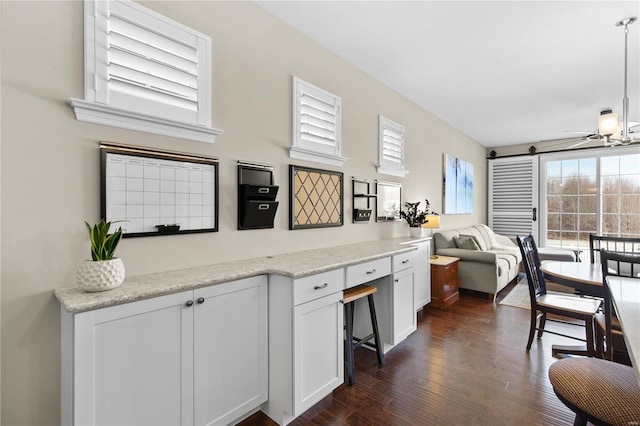 kitchen with white cabinets, hanging light fixtures, ceiling fan, light stone countertops, and dark wood-type flooring