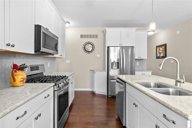 kitchen with appliances with stainless steel finishes, sink, white cabinets, decorative backsplash, and hanging light fixtures