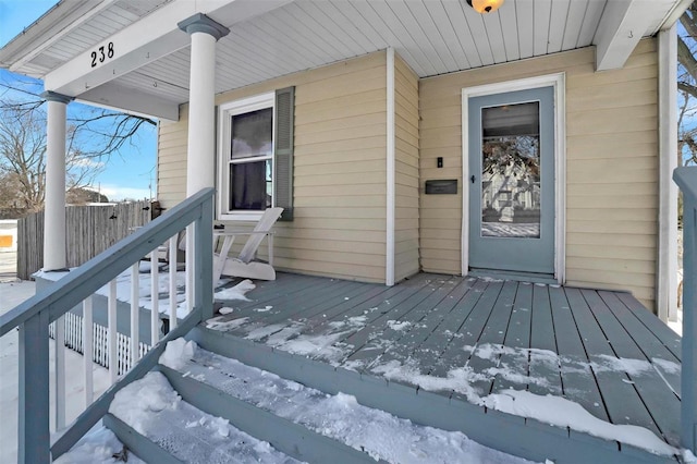 snow covered property entrance with covered porch and fence