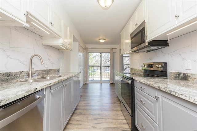 kitchen with light wood-type flooring, a sink, tasteful backsplash, appliances with stainless steel finishes, and white cabinets