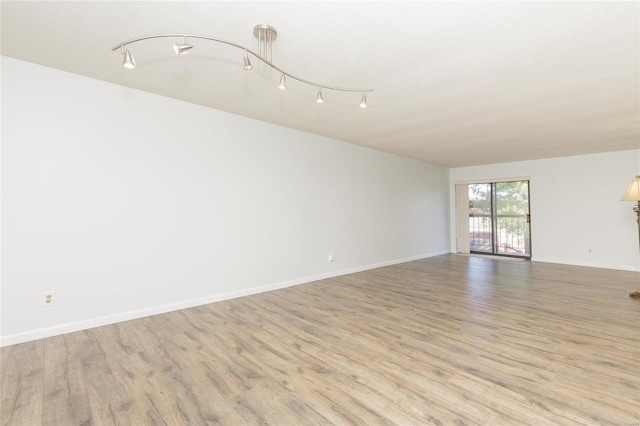 empty room featuring track lighting, light wood-type flooring, and baseboards