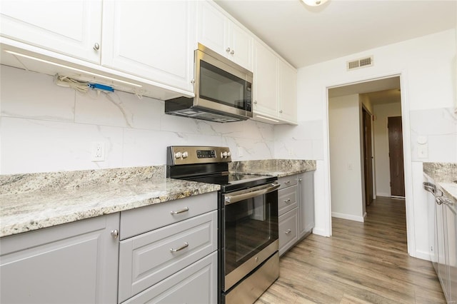 kitchen with visible vents, white cabinets, light wood-style floors, appliances with stainless steel finishes, and backsplash