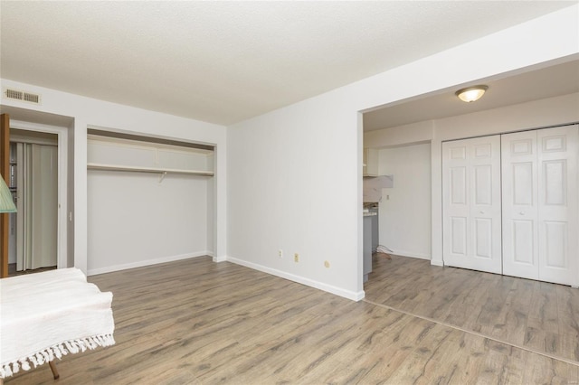 unfurnished bedroom with a textured ceiling, wood finished floors, visible vents, and baseboards