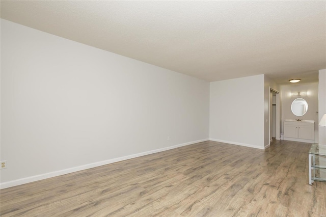 unfurnished room featuring baseboards, light wood finished floors, and a textured ceiling