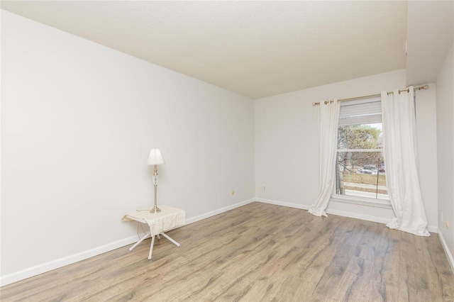 spare room with baseboards and wood finished floors