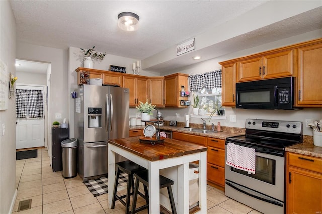 kitchen featuring sink, light tile patterned floors, light stone counters, stainless steel appliances, and a textured ceiling