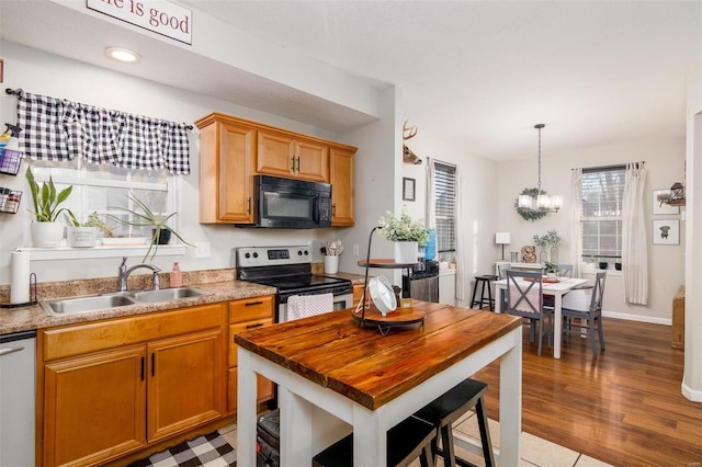 kitchen featuring pendant lighting, sink, appliances with stainless steel finishes, a notable chandelier, and light wood-type flooring