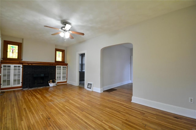 unfurnished living room with ceiling fan, a brick fireplace, and light hardwood / wood-style floors