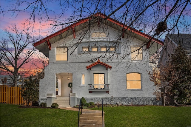 view of front of property featuring a balcony, fence, and a lawn