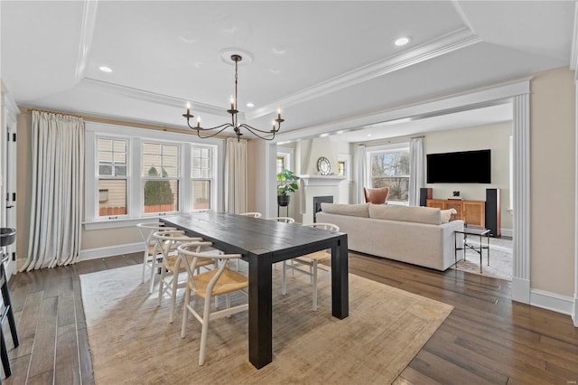 dining space featuring a tray ceiling, a fireplace, wood finished floors, and crown molding