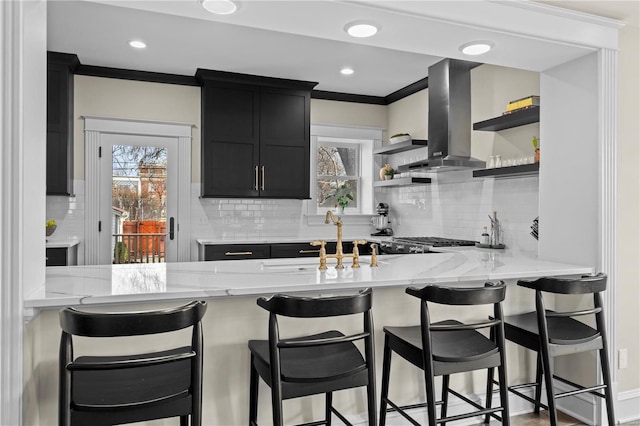 kitchen with a sink, a kitchen breakfast bar, dark cabinetry, open shelves, and island exhaust hood