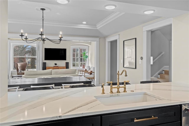 kitchen with light stone counters, dark cabinets, decorative light fixtures, crown molding, and a sink