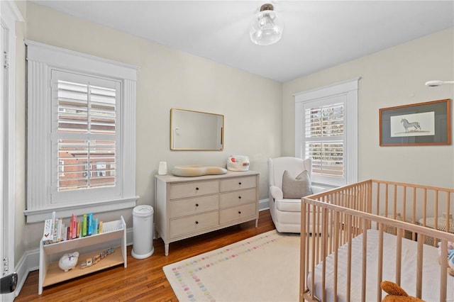 bedroom featuring a crib, light wood-style flooring, and baseboards