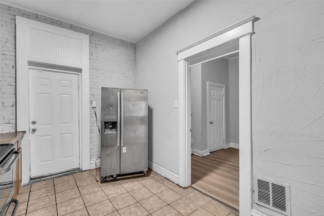 kitchen with brick wall, stainless steel fridge, light tile patterned floors, and stove