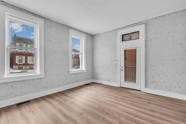 unfurnished room featuring light hardwood / wood-style floors and brick wall