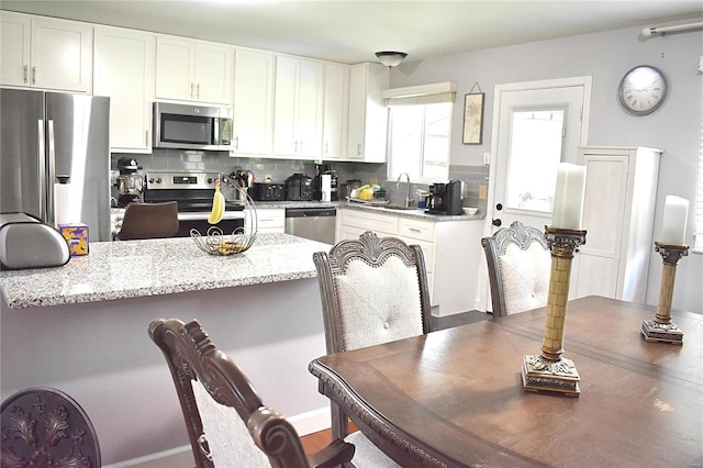 kitchen with stainless steel appliances, backsplash, white cabinets, and light stone counters