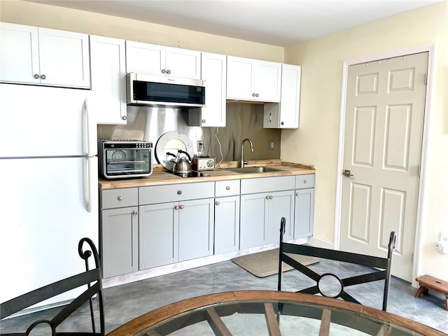 kitchen featuring a sink, white cabinets, light countertops, freestanding refrigerator, and stainless steel microwave