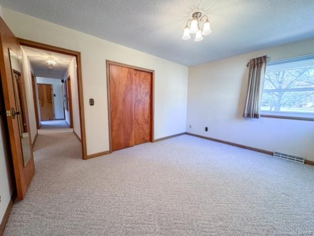 unfurnished bedroom with a textured ceiling, an inviting chandelier, light carpet, and a closet