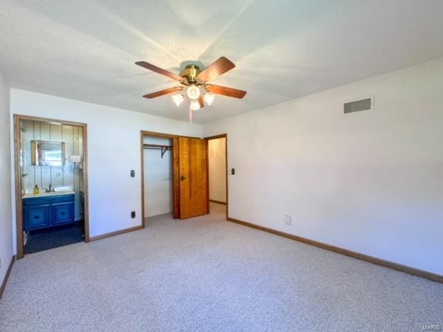 unfurnished bedroom with a closet, connected bathroom, ceiling fan, sink, and light colored carpet