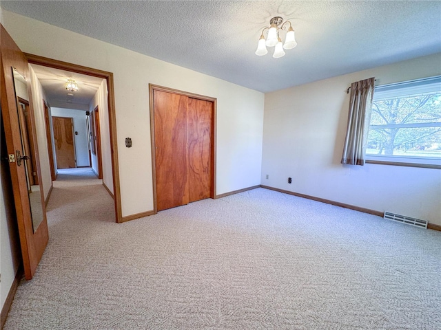 unfurnished bedroom with a chandelier, a closet, a textured ceiling, and light colored carpet