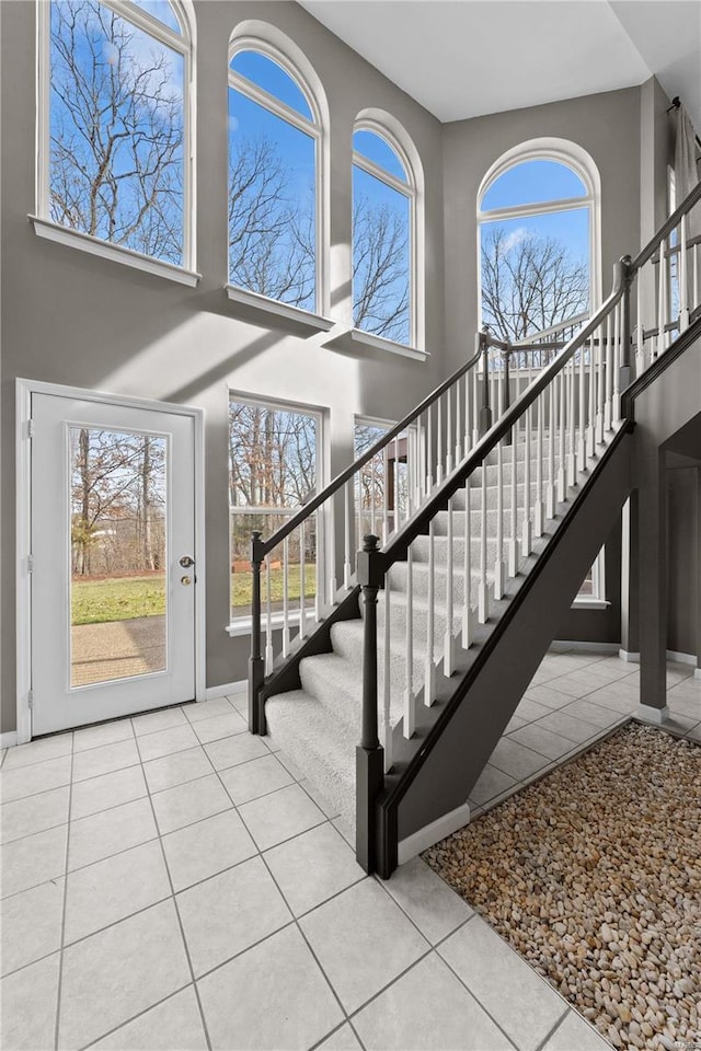 stairway with a towering ceiling, tile patterned floors, and plenty of natural light