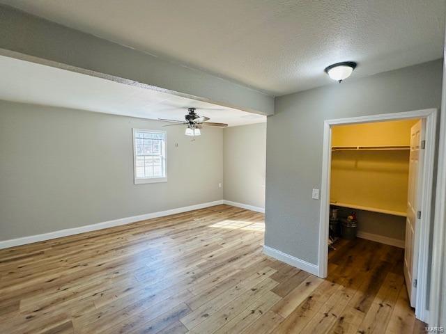 unfurnished bedroom with a closet, a walk in closet, a textured ceiling, and light hardwood / wood-style flooring