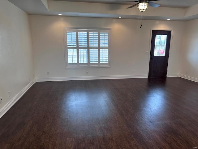 unfurnished room featuring a tray ceiling, dark hardwood / wood-style floors, and ceiling fan