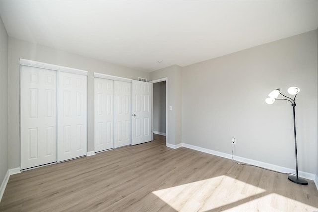 unfurnished bedroom featuring light wood-type flooring and two closets