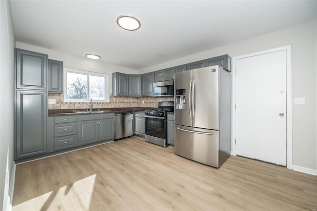 kitchen with sink, light hardwood / wood-style flooring, gray cabinetry, backsplash, and stainless steel appliances