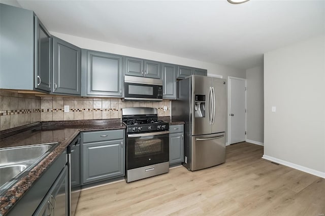 kitchen with sink, appliances with stainless steel finishes, gray cabinetry, backsplash, and light wood-type flooring