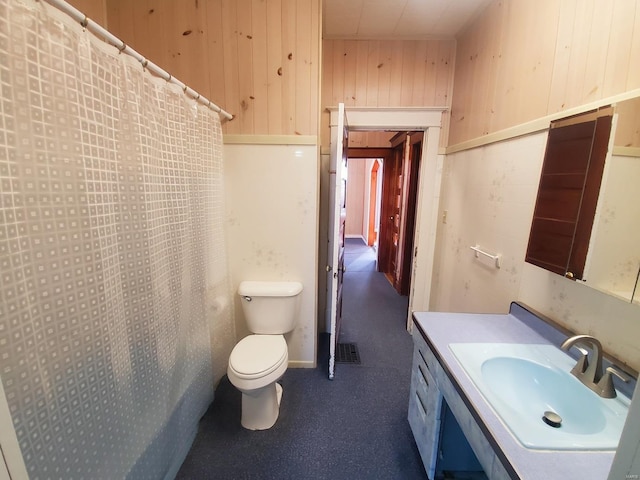 bathroom featuring vanity, wooden walls, toilet, and walk in shower