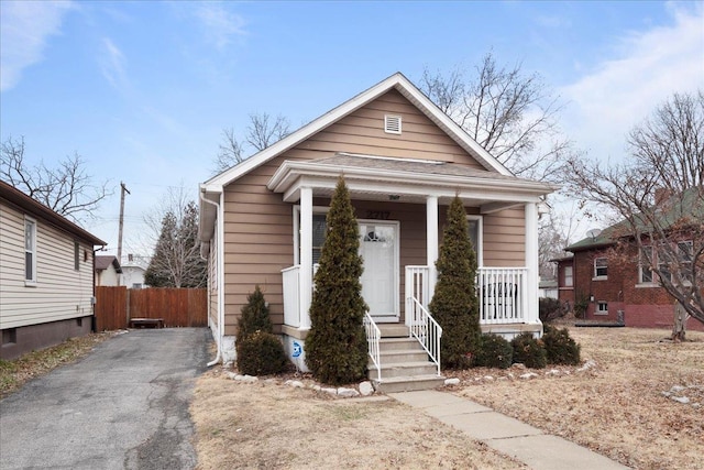 view of front facade featuring a porch, fence, and aphalt driveway