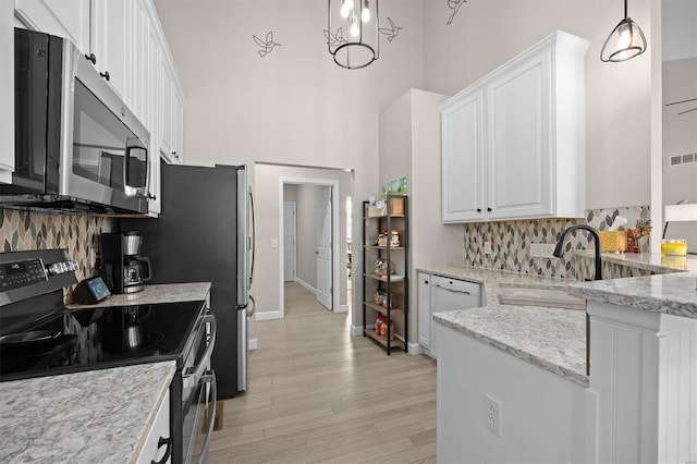 kitchen with white cabinetry, stainless steel appliances, light stone counters, and hanging light fixtures